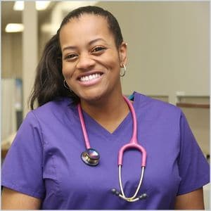 healthcare worker doctor female nurse smiling in purple scrubs with a pink stethoscope around her neck