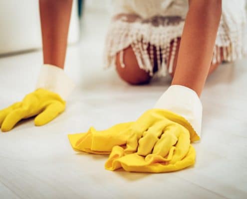 Person cleaning a white tile floor with a rag wearing rubber gloves