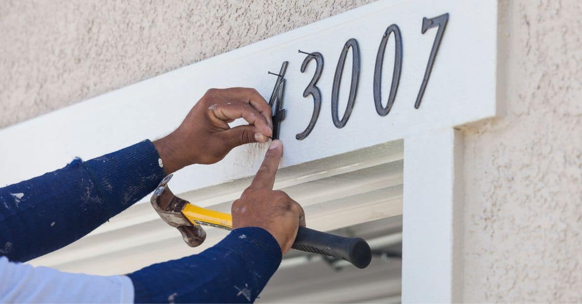 Man Holding Hammer Nail Adding Address Numbers to Side of Home