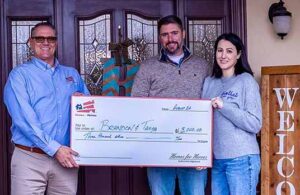 couple holding big check of savings with Homes for Heroes real estate specialist in front of new home 540x350