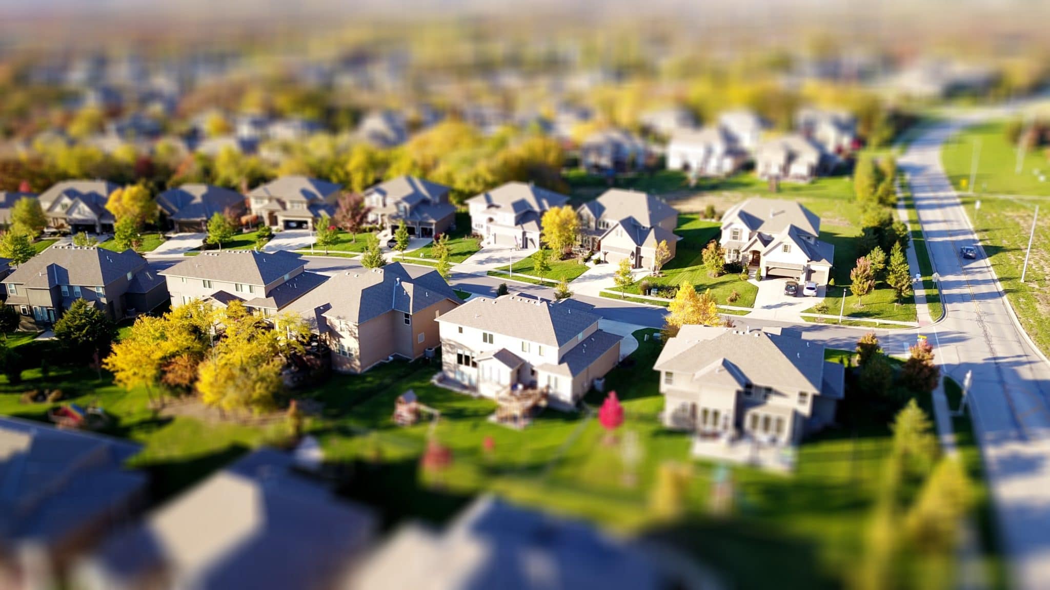 A suburban neighborhood in an areal shot with a street of houses sharp in the middle with the surrounding picture blurred.