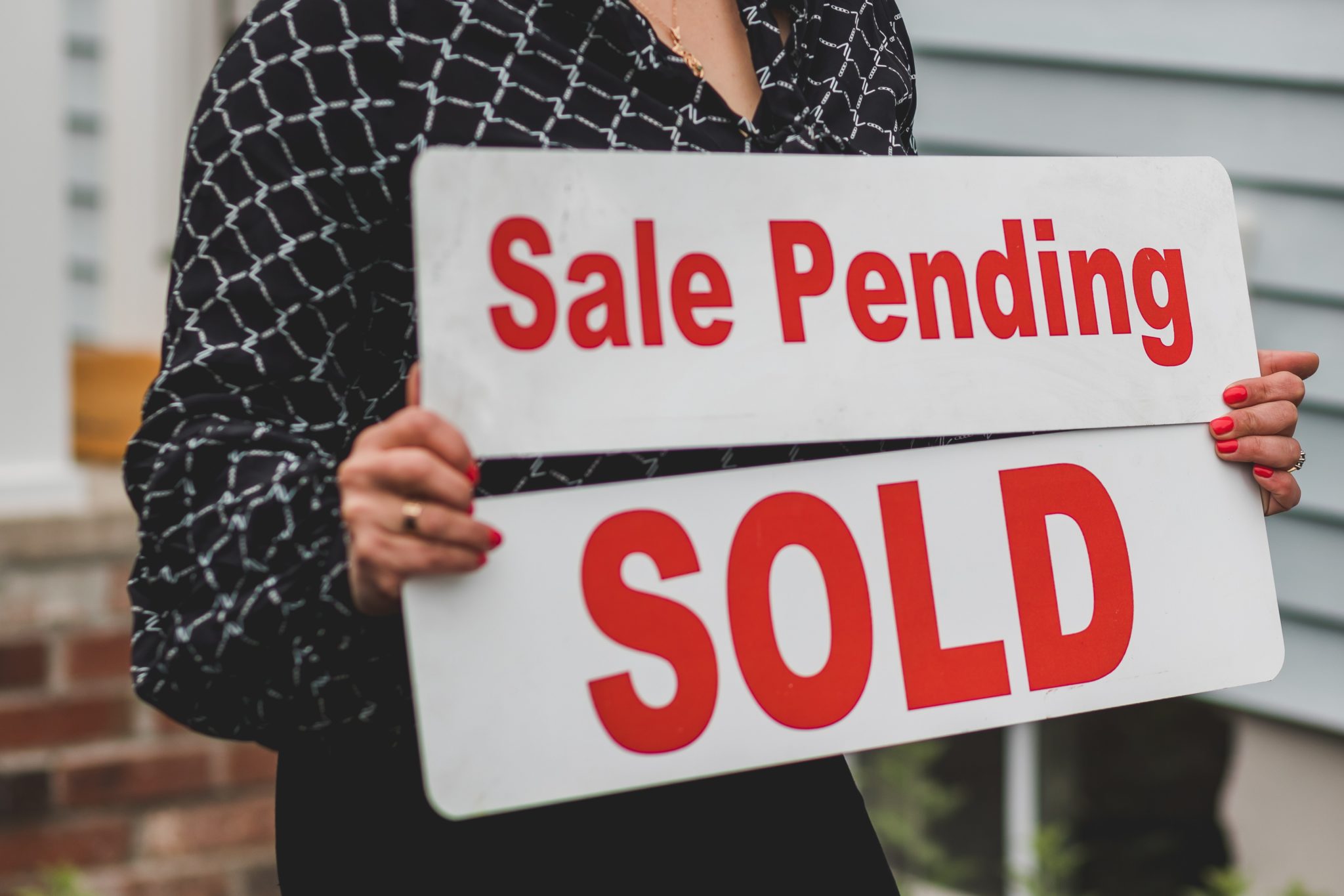 A woman real estate agent holds two signs, one that says sale pending and the other says sold.