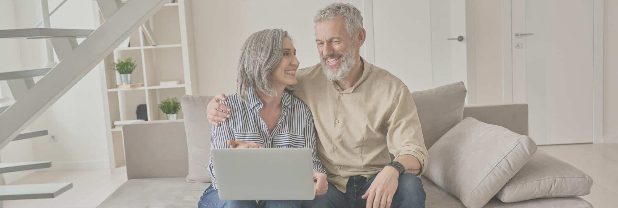 Mature couple senior couple sitting on couch looking at laptop at home talking downsize house