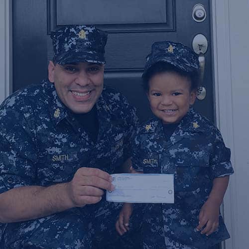 Military father kneeling down with son both in uniform in front of house holding Homes for Heroes Hero Rewards Savings check