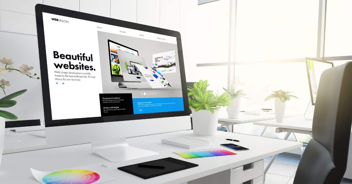white desk with monitor featuring website design with color cards to determine website brand identity elements for new real estate website