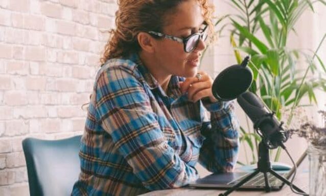 female real estate agent sitting in office at desk with microphone laptop recording real estate video about current market conditions