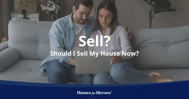 young couple sitting couch in living room discussing should i sell my house now looking at laptop doing research Homes for Heroes