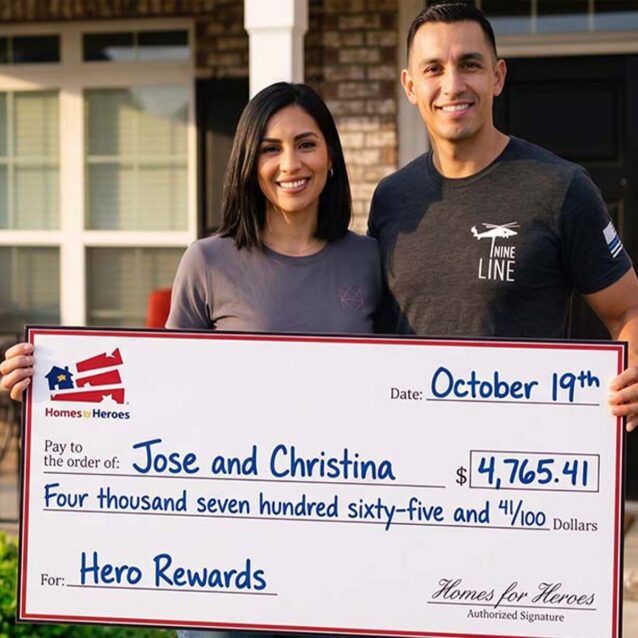 Jose, wearing a law enforcement-themed shirt, and Christina smiling while holding a Homes for Heroes check for $4,765.41 in front of their residence.